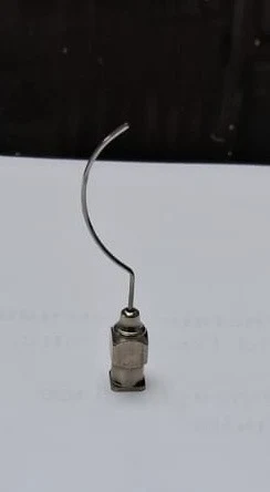 The same cannula stood upright on its hub, showing the curve of the shaft in profile against a plain background.